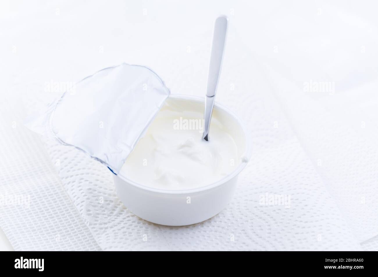 Yogurt greco semplice in tazza con cucchiaio su sfondo bianco Foto Stock