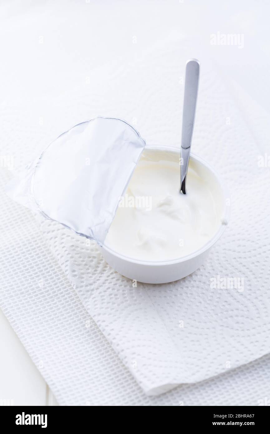 Yogurt greco semplice in tazza con cucchiaio su sfondo bianco Foto Stock
