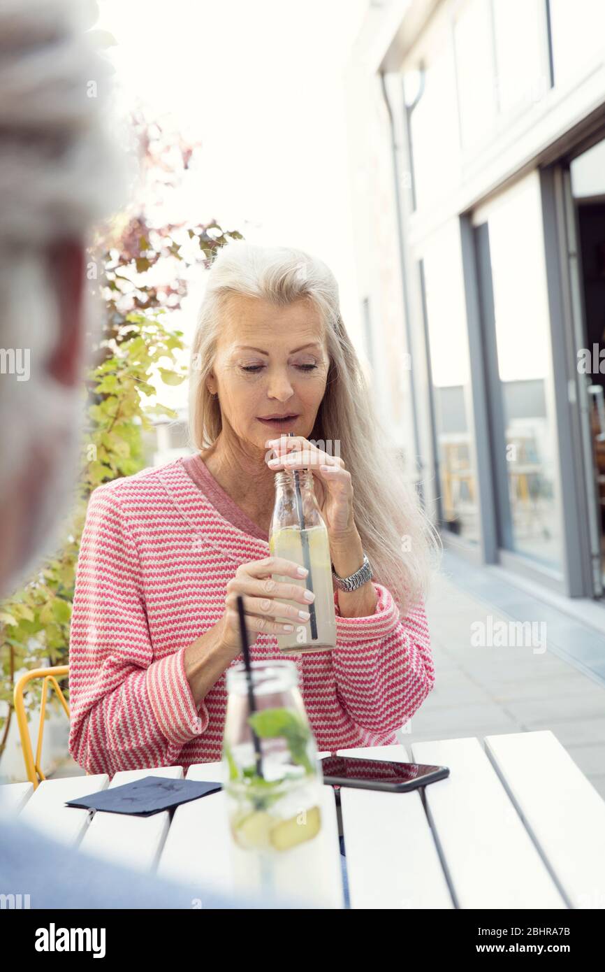 Una coppia seduta al tavolo, la donna di fronte alla macchina fotografica e bere da una bottiglia con una cannuccia. Foto Stock