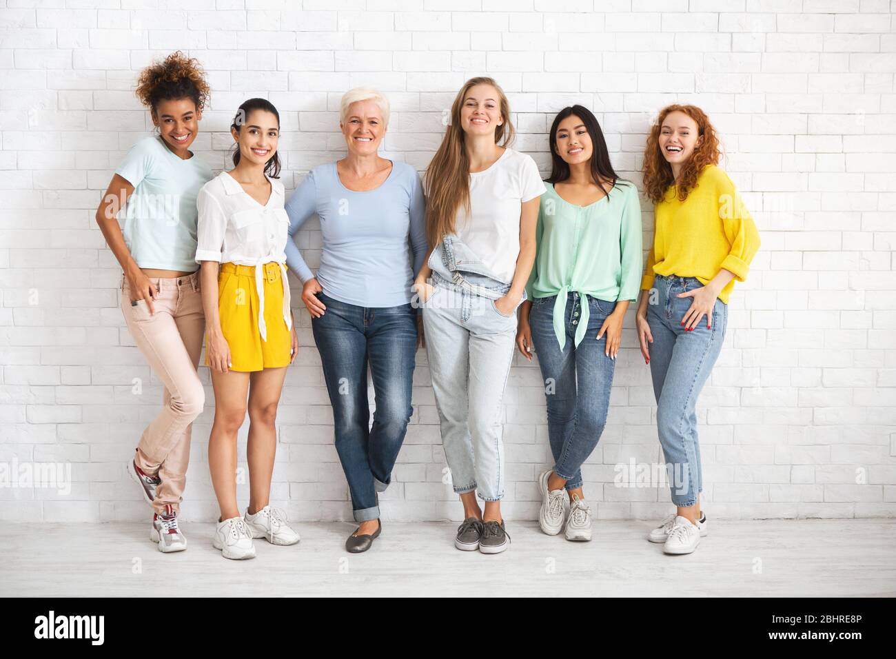 Diverse donne di età diversa in piedi sul muro di mattoni bianchi Foto Stock