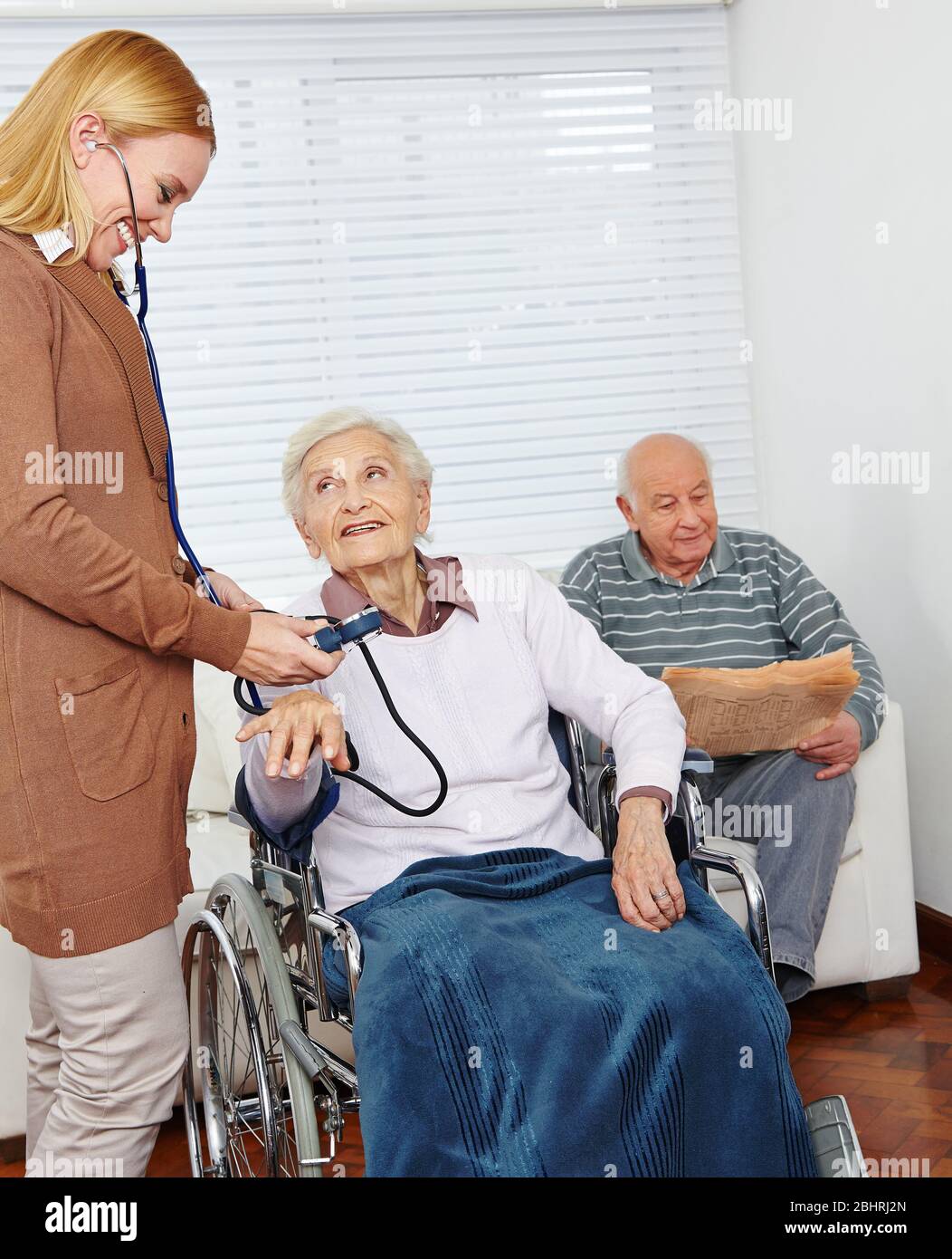 Donna del servizio infermieristico misura la pressione sanguigna nelle donne anziane in sedia a rotelle a casa Foto Stock