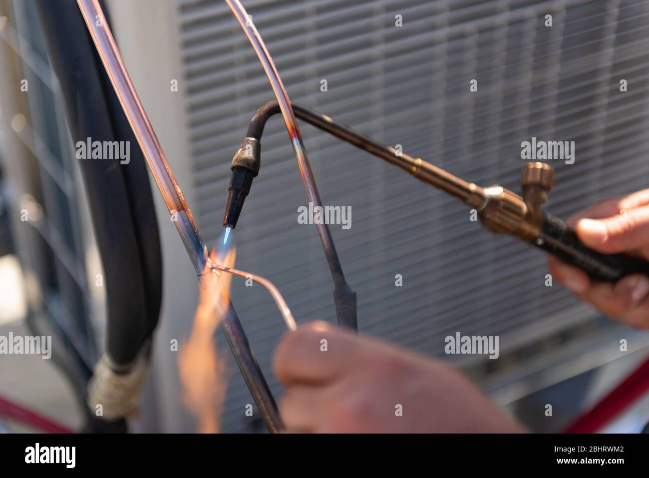 Il tecnico HVAC sta lavorando sulle unità di condizionamento dell'aria su un tetto di nuovo edificio industriale. Immagine a segmenti del tecnico HVAC che salda il giunto di rame Foto Stock