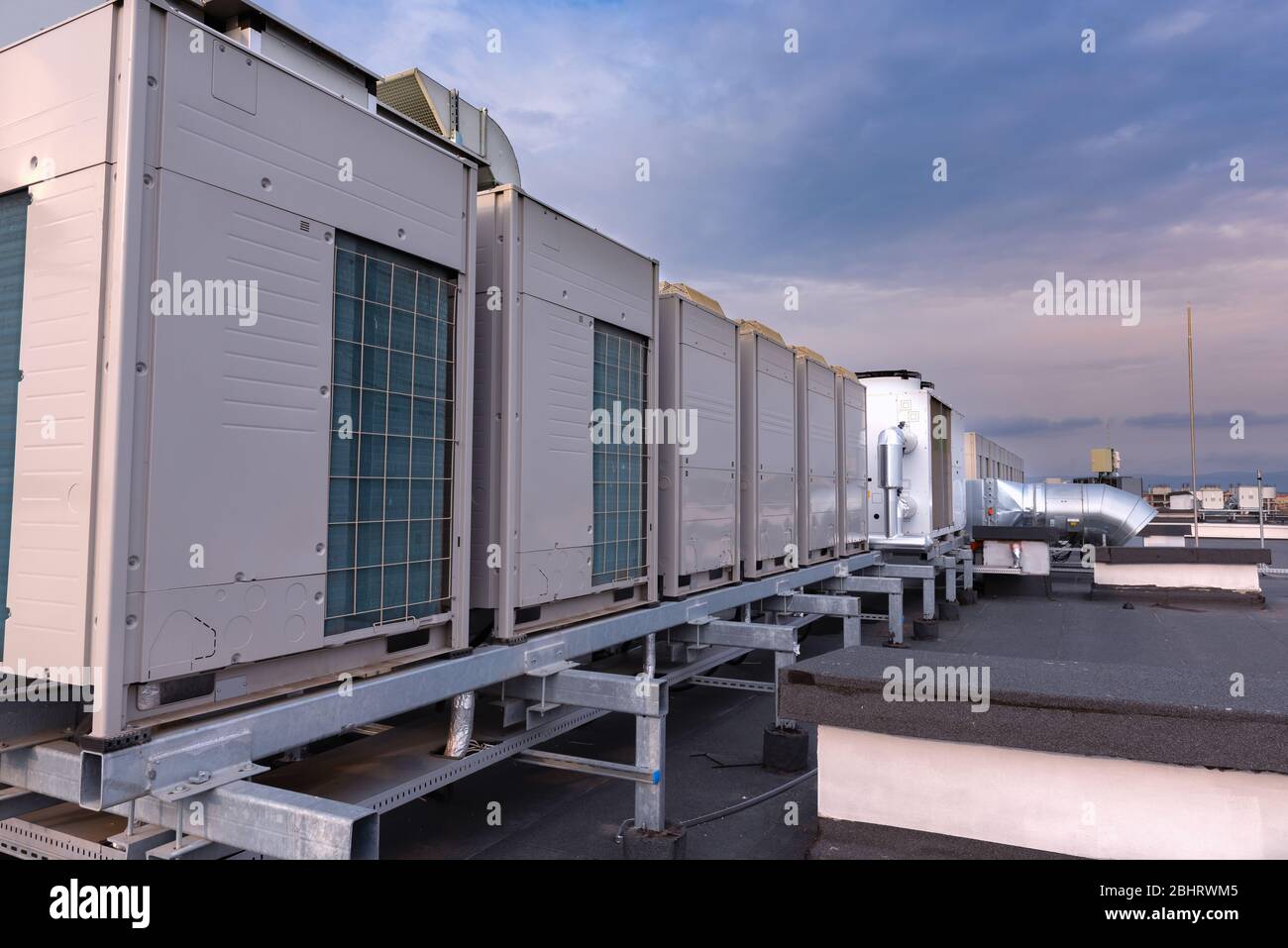 Unità di aria condizionata VRV HVAC, grande ventilatore e un radiatore dell'acqua su un tetto di nuovo edificio industriale con cielo blu e nuvole sullo sfondo. Foto Stock