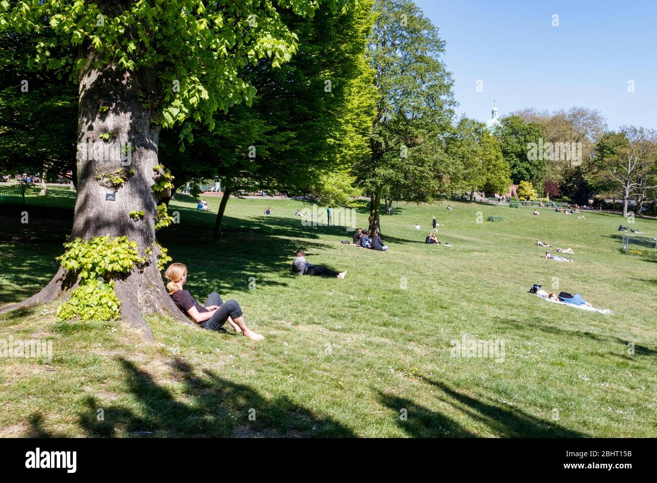 Persone che si rilassano e prendono il sole nel parco, osservando le distanze sociali, durante la pandemia di coronavirus, Londra, Regno Unito Foto Stock