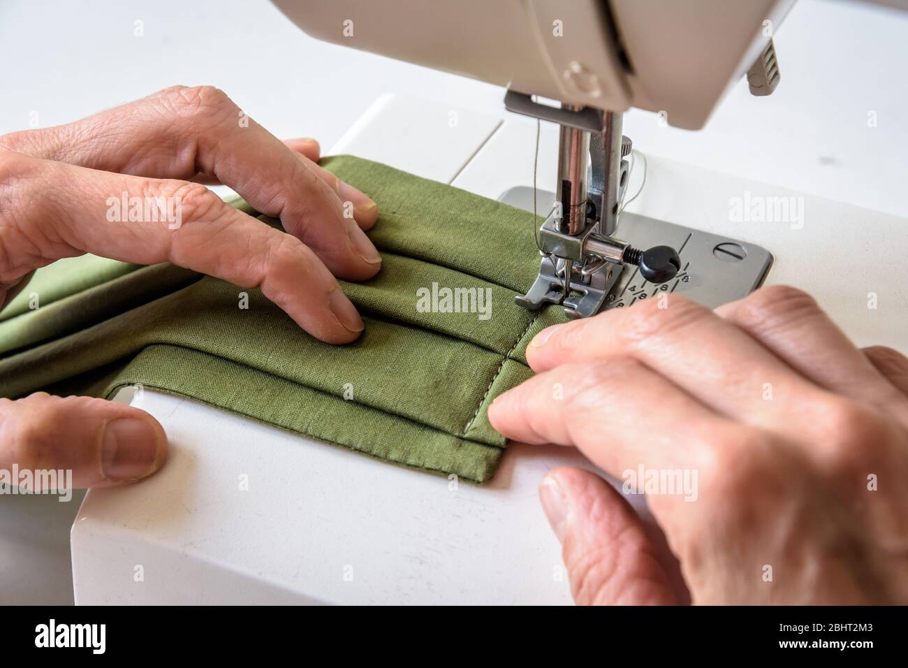Vista ravvicinata sulle mani di una donna che cucita su una macchina da cucire i rivestimenti del viso in tessuto di cotone verde. Foto Stock