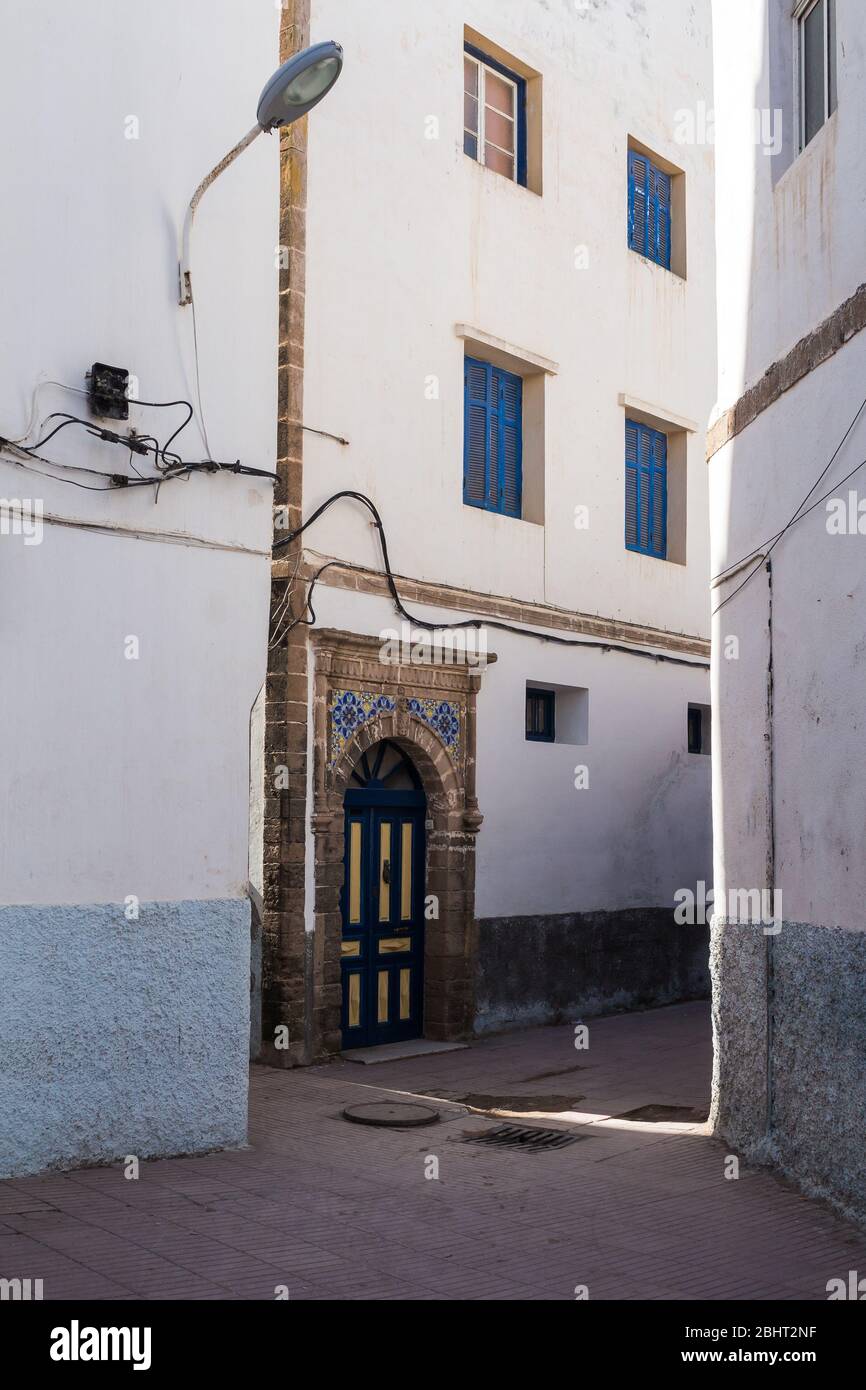 Strada stretta con case con piccole finestre e persiane blu. Tradizionale facciata bianca. Centro storico (medina) di Essaouira, Morocoo. Foto Stock