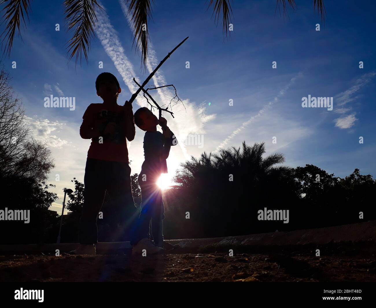 Silhouette di due bambini retroilluminati che giocano all'aperto contro un cielo blu. Foto Stock