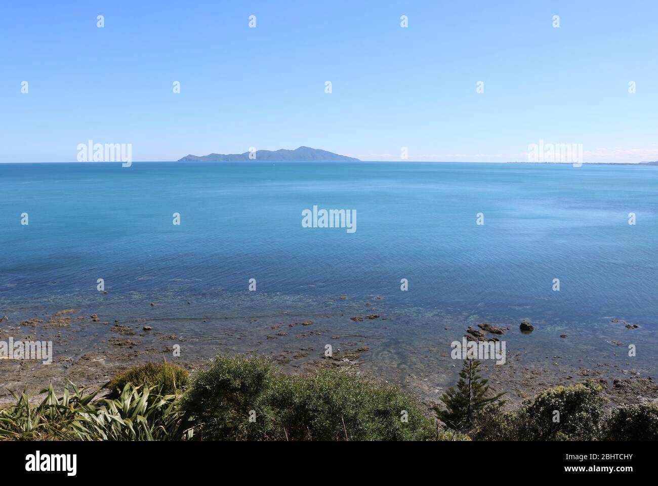 Guardando a nord da Pukerua Bay sulla costa occidentale di North Island, Nuova Zelanda attraverso il mare di Tasman a Kapiti Island in una limpida giornata soleggiata di novembre. Foto Stock