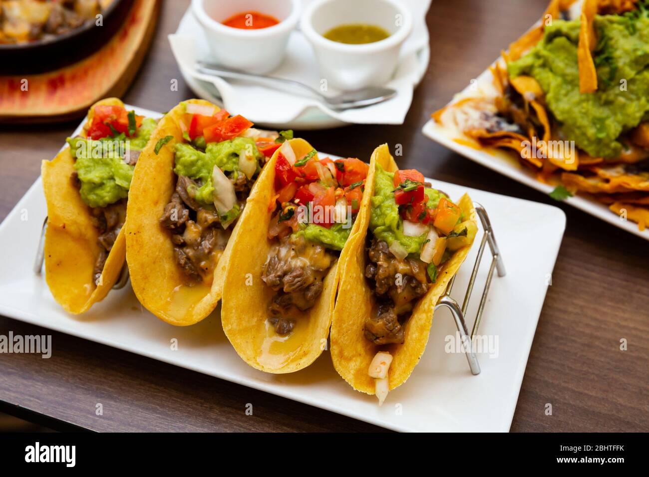 Deliziosi tacos messicani di tortillas di mais con carne di manzo arrosto,  guacamole, verdure fresche, verdure servite con due salse Foto stock - Alamy