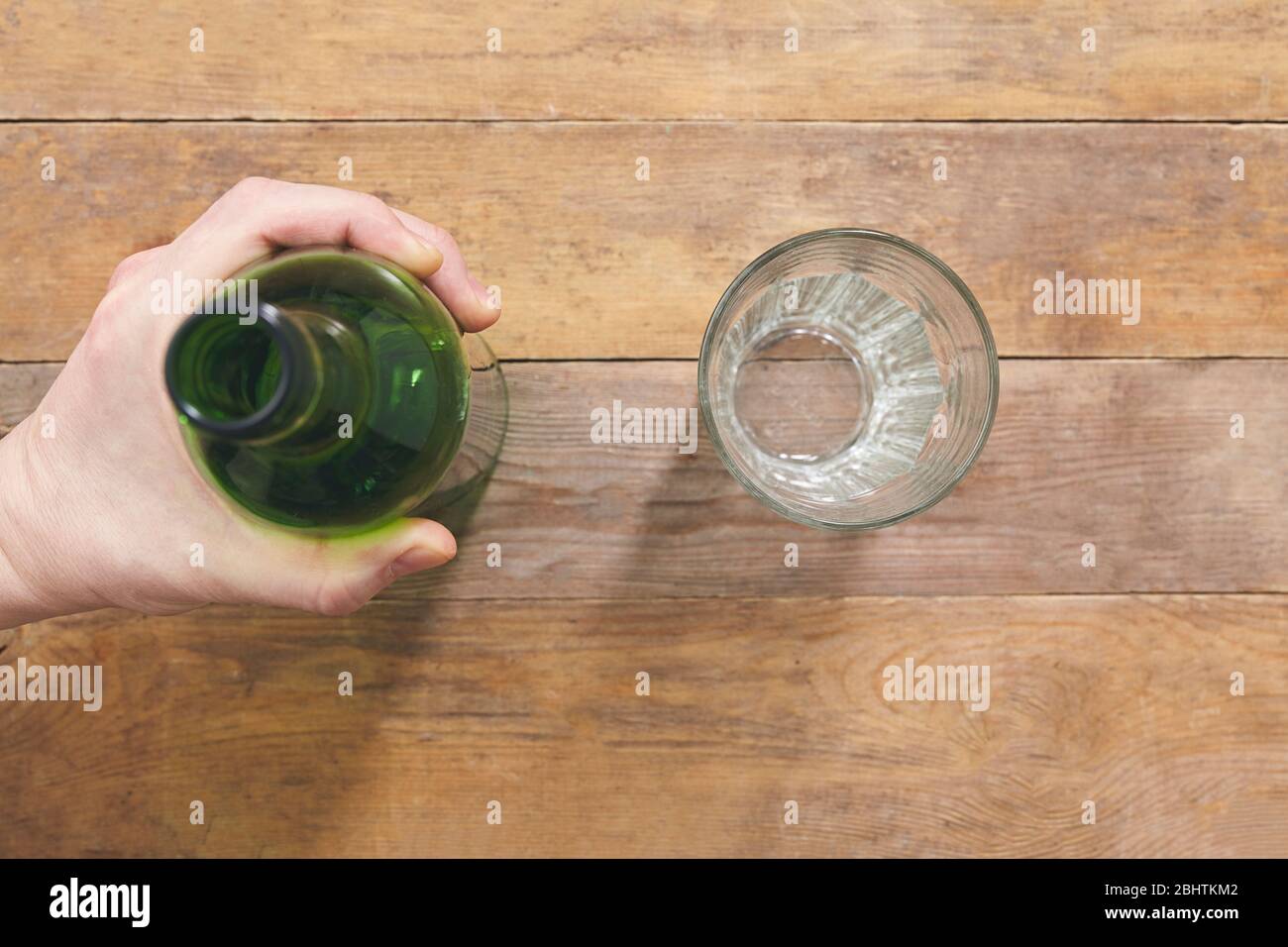 Tenere la bottiglia a mano su tavolo di legno con vetro. Vista dall'alto. Foto Stock