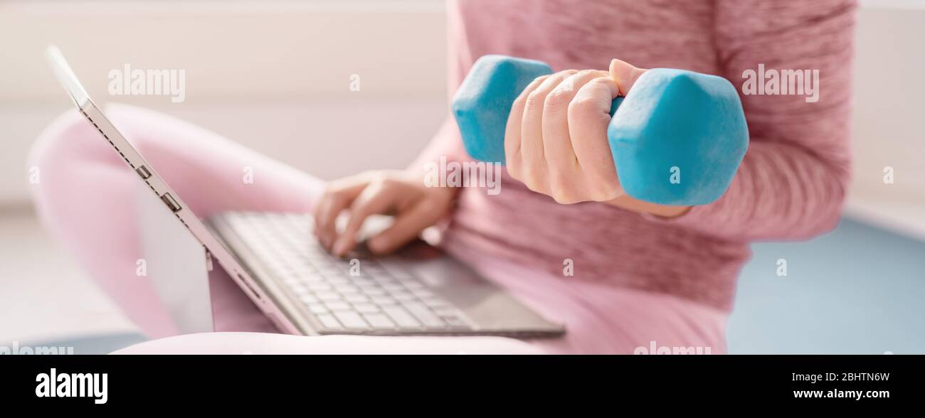 Donna che usa il laptop a casa guardando i video di fitness allenamento online con il peso di manubri. Misura la ragazza utilizzando pesi che lavorano le braccia banner panoramico. Foto Stock