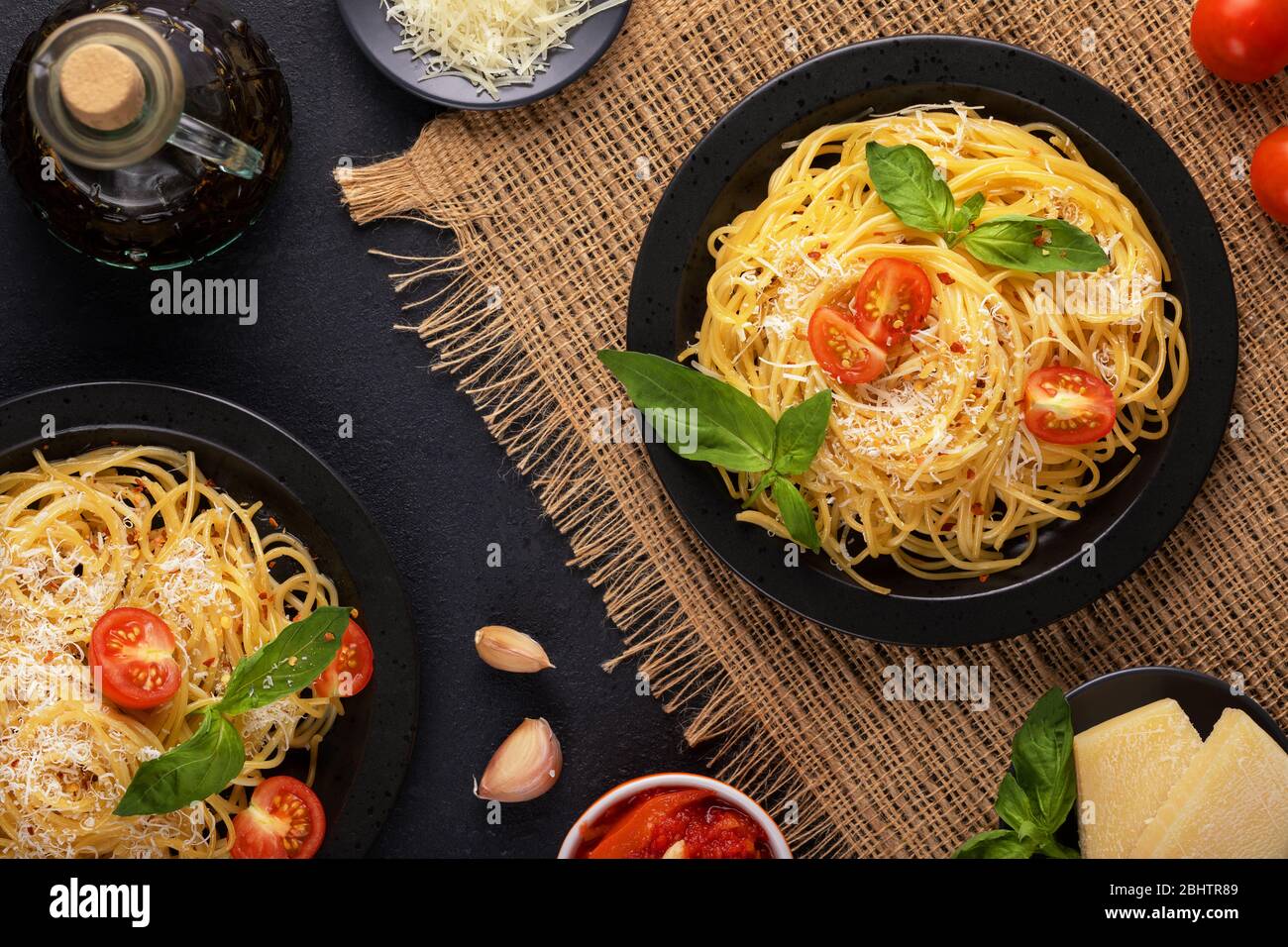 Due piatti neri con verdure vegetariane, gustosi spaghetti classici italiani con basilico, salsa di pomodoro, parmigiano e olio d'oliva al burlap su un Foto Stock