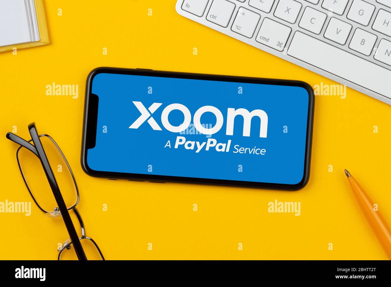 Uno smartphone con il logo Xoom è posizionato su uno sfondo giallo insieme a tastiera, occhiali, penna e libro (solo per uso editoriale). Foto Stock