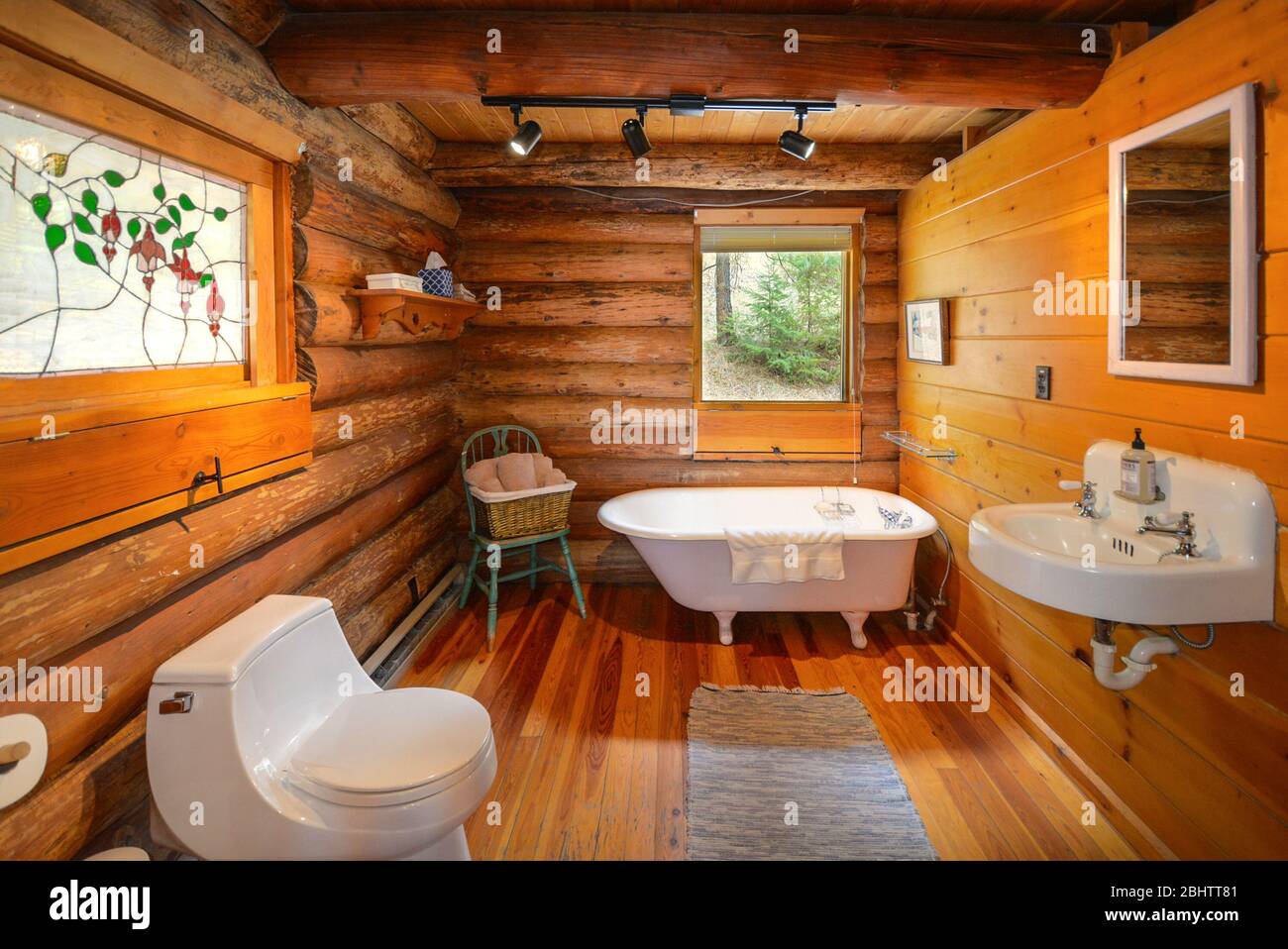 Un bagno in una casa rustica di legno di montagna con lavandino, servizi igienici e vasca da bagno plantare. Foto Stock