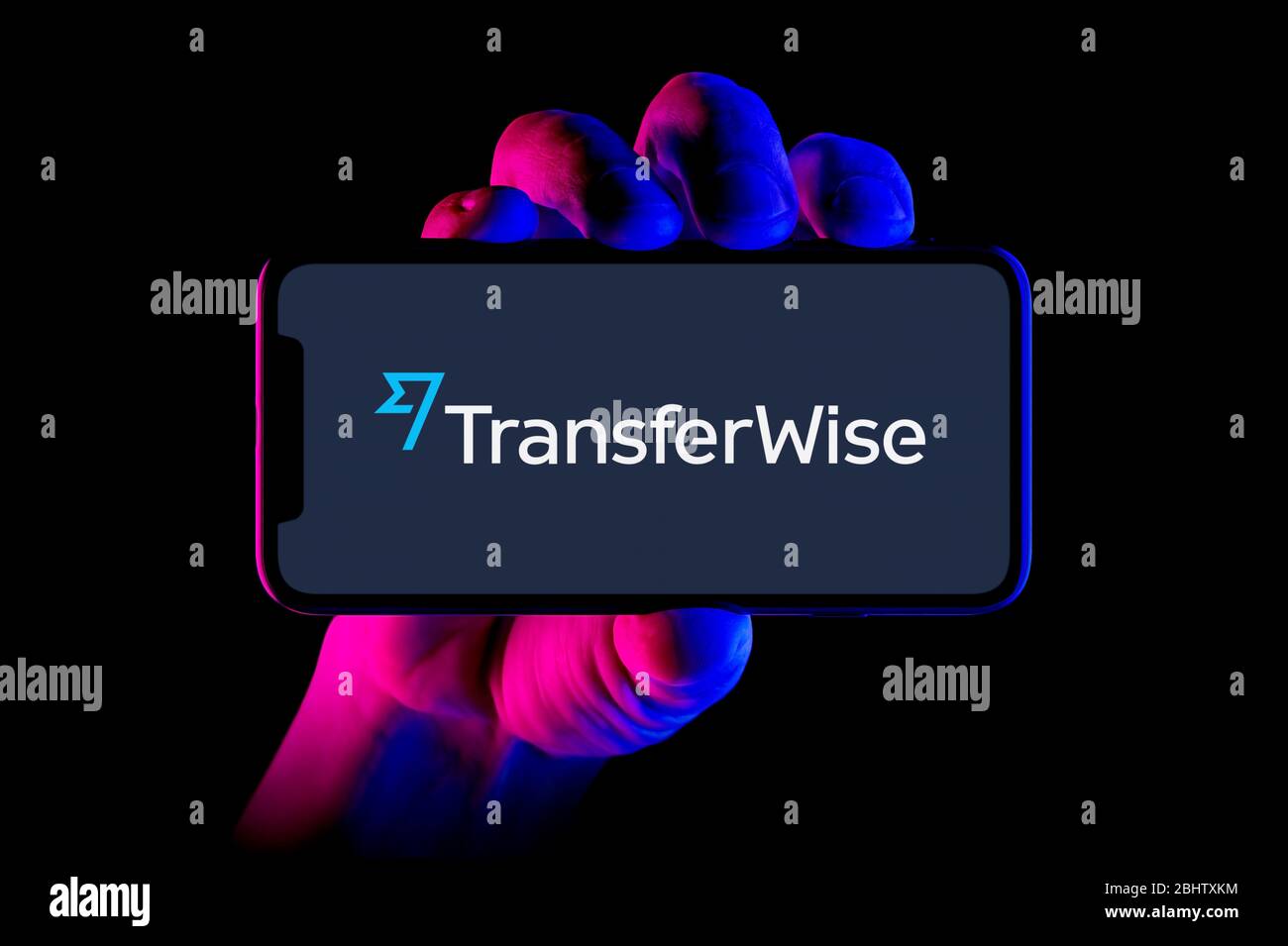 Uno smartphone con il logo Transferwise è tenuto da un colpo a mano su sfondo nero (solo per uso editoriale). Foto Stock