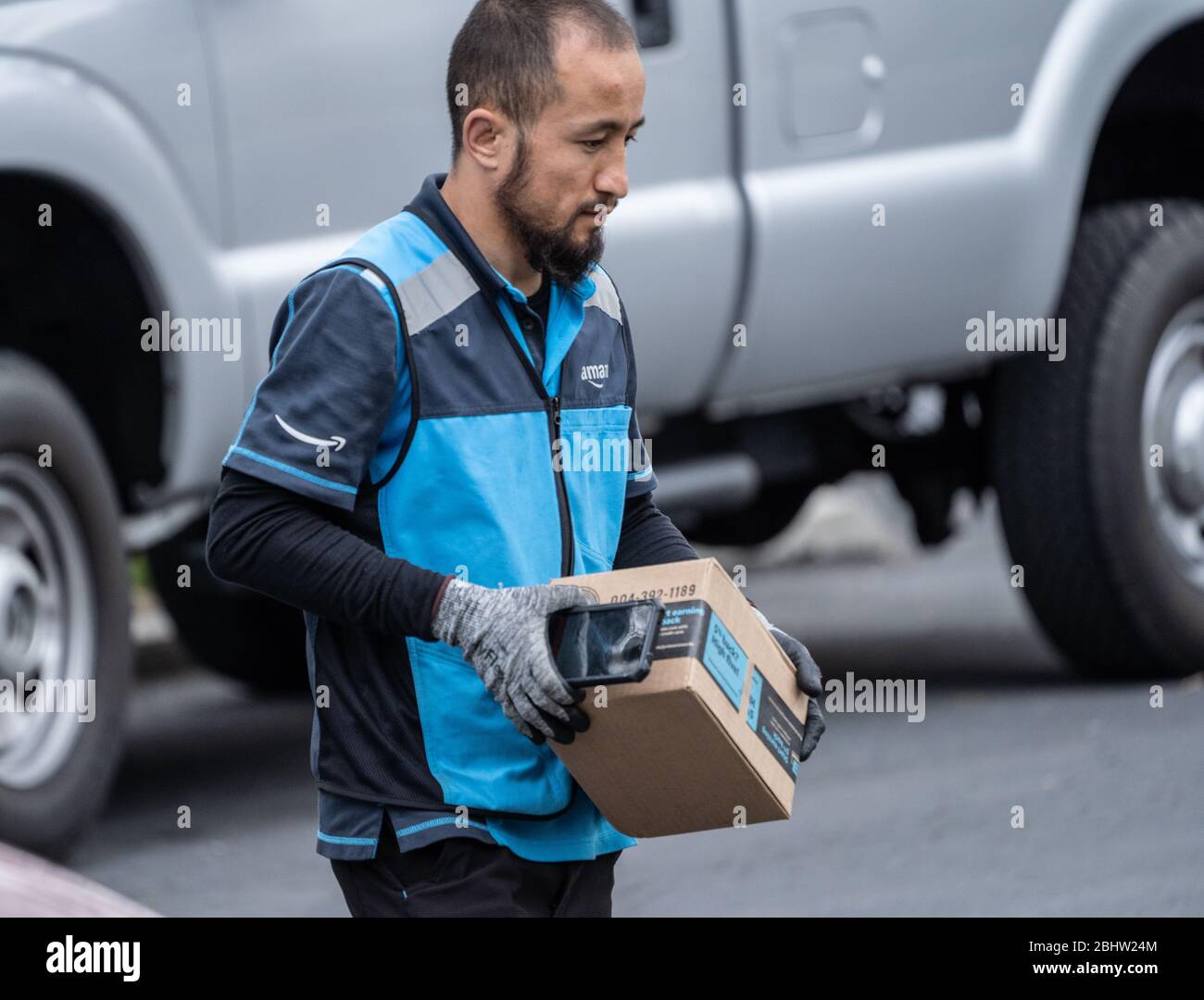 Berks County, Pennsylvania, USA, 26 aprile 2020-persona di consegna Amazon che indossa i pacchetti di guanti sulla strada suburbana Foto Stock