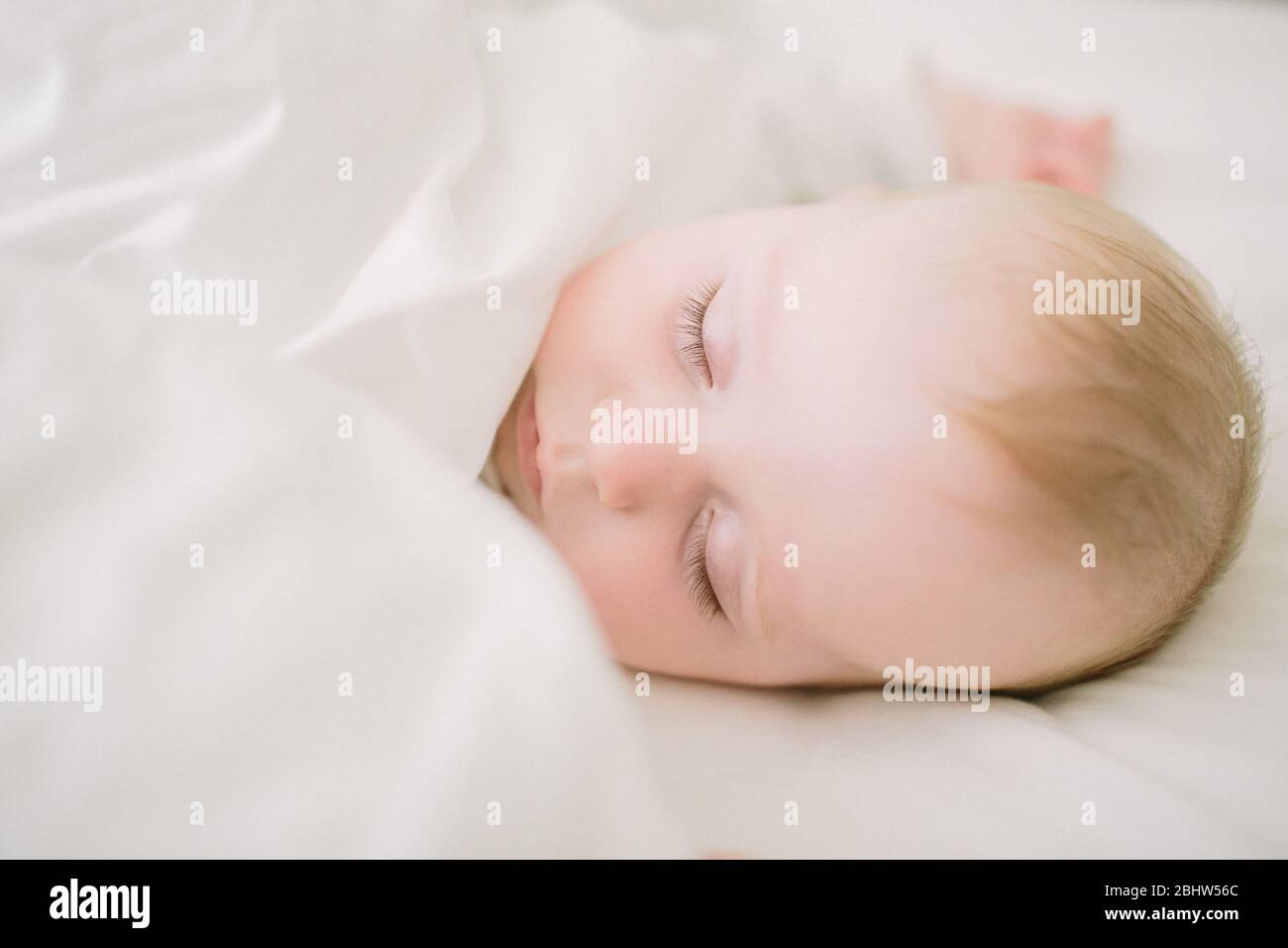 Sonno tranquillo ed etereo bambino circondato da coperta bianca Foto Stock