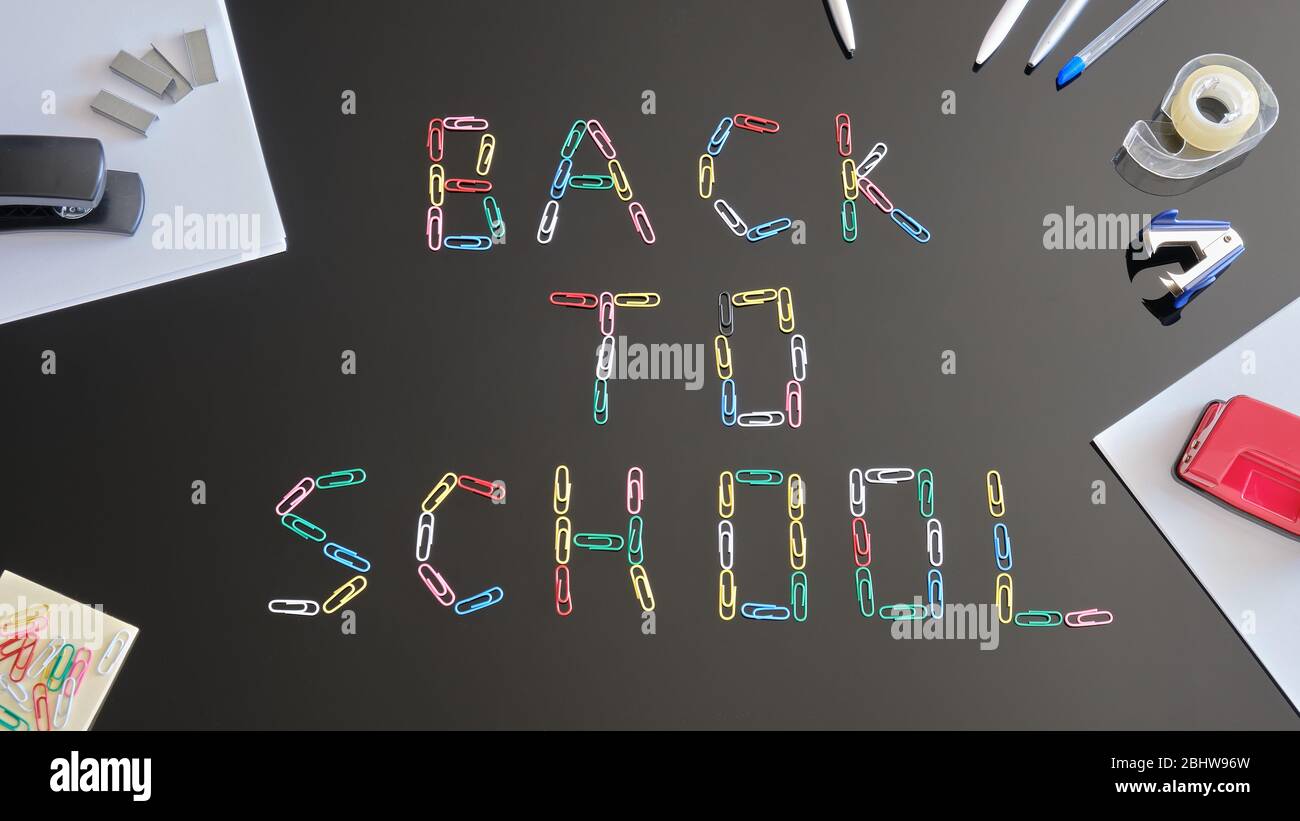 Concetto di ritorno a scuola - composizione di laici piatti. Graffette che formano le parole su un tavolo nero riflessivo, circondato da fogli di carta e scuola relativa Foto Stock