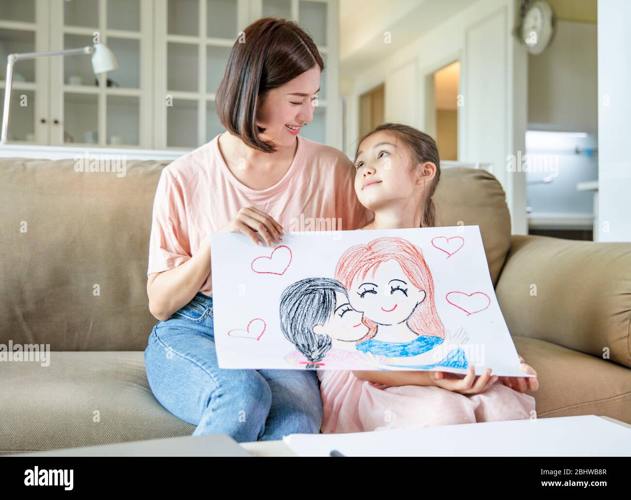 Bambina che mostra colore matita disegno immagine di famiglia alla sua madre e celebrando il giorno delle madri Foto Stock