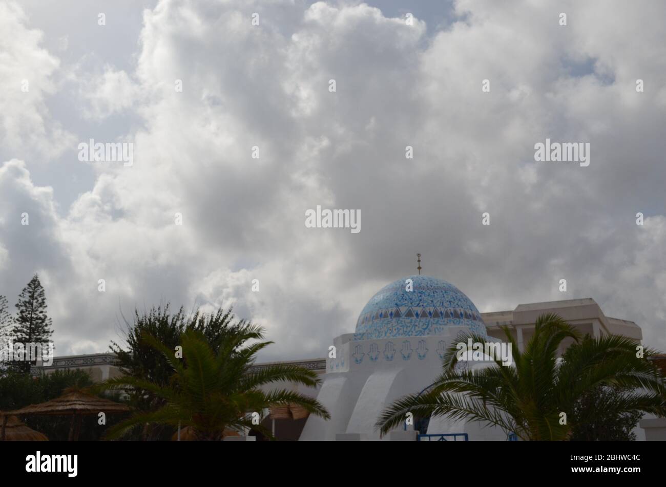 un bel colpo di un edificio islamico decorato da una massa enorme di nuvole e alcune palme. Foto Stock