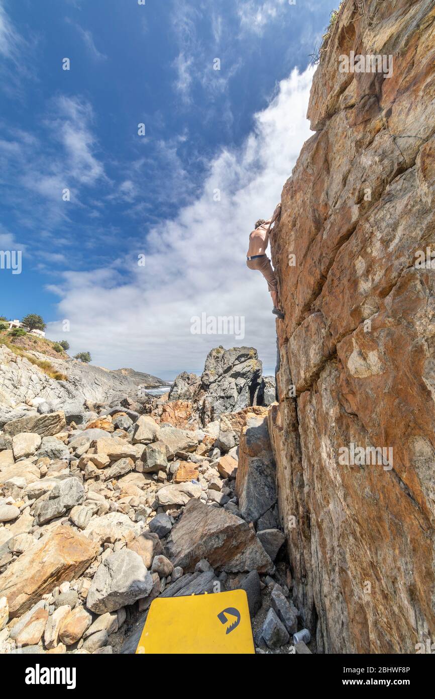 Scalatore di roccia maschile che pratica bouldering senza corda su un'area di masso di fronte al mare. Un masso elevato per persone con tenacia e fiducia Foto Stock