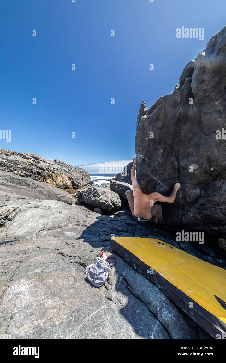 Scalatore di roccia maschile che pratica bouldering senza corda su un'area di masso di fronte al mare. Un masso elevato per persone con tenacia e fiducia Foto Stock