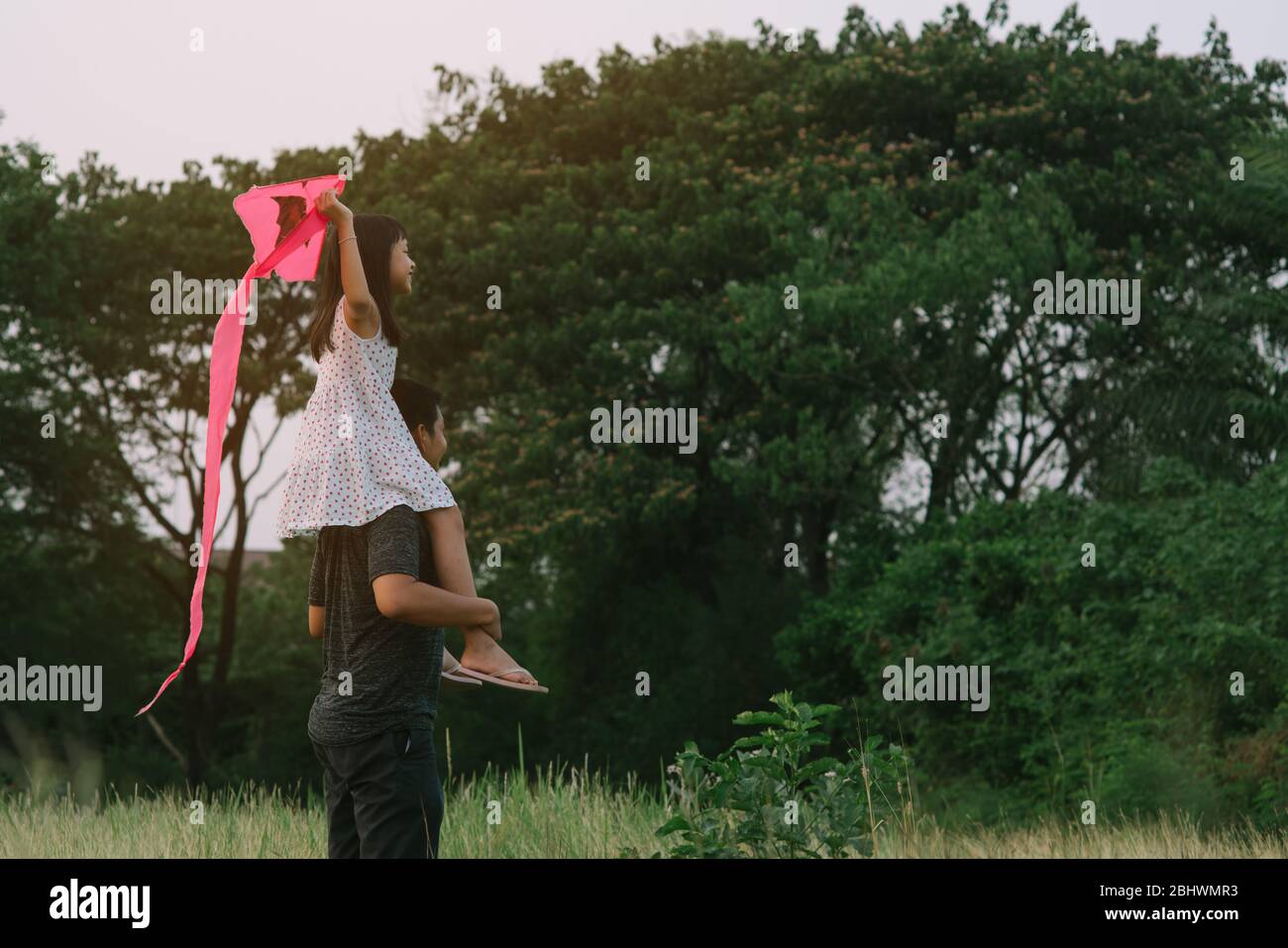 Bambina asiatica cavalcando sulle spalle del padre in verde sfondo naturale con la tenuta dello stile kite.16:9 Foto Stock