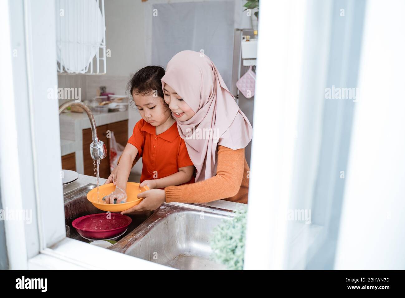 Aiuto mano. Cute Little Girl aiuta la sua madre musulmana nel lavare i piatti alla cucina di famiglia Foto Stock