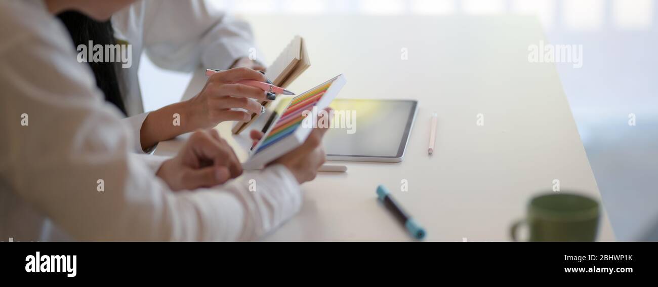 Vista laterale del team di designer che consulta il loro progetto su un tavolo bianco con forniture di designer e un mock-up tablet Foto Stock