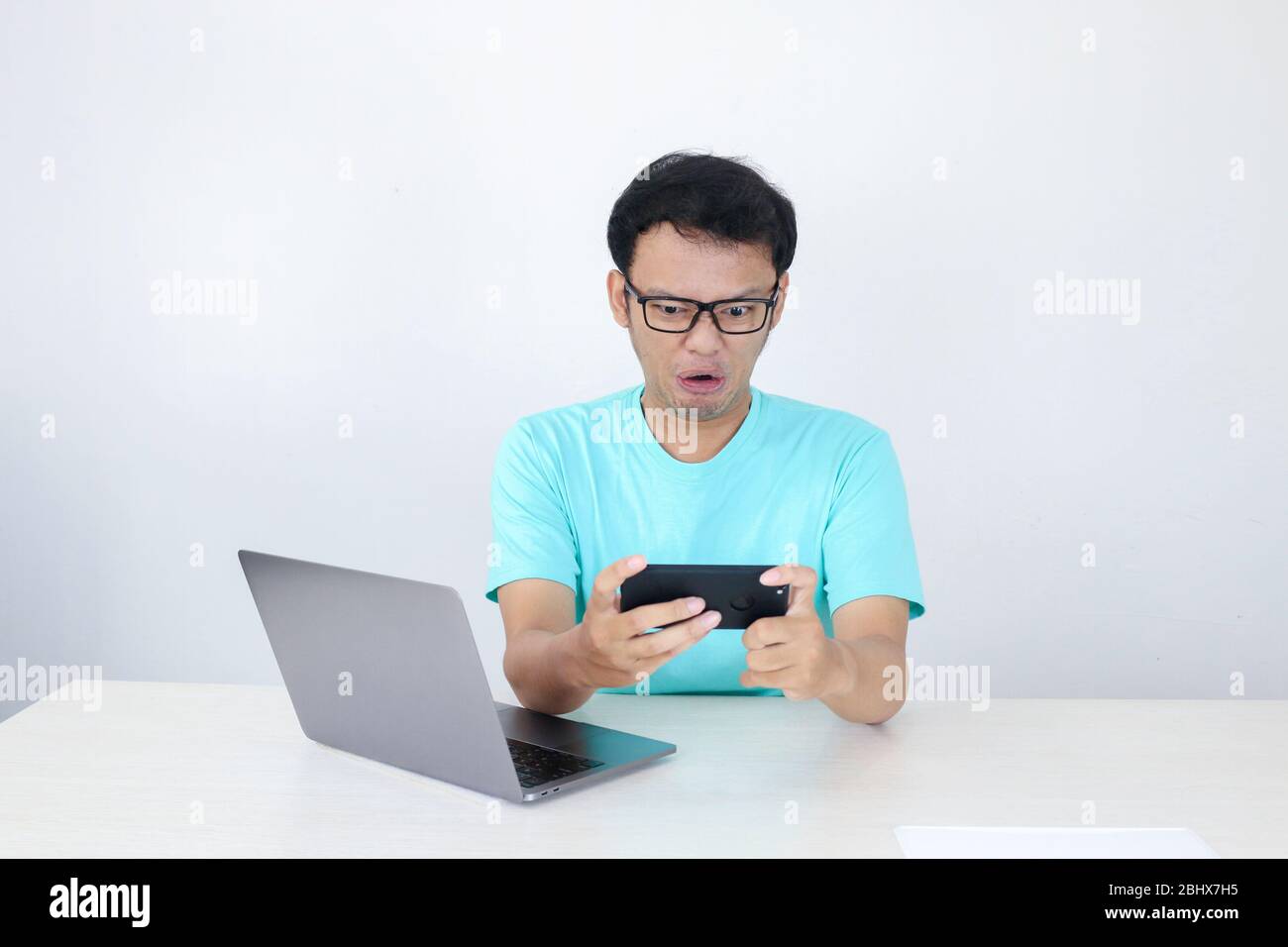 Un giovane asiatico arrabbiato si impazzisce sullo smartphone quando gioca  al lavoro. Uomo indonesiano che indossa una camicia blu Foto stock - Alamy