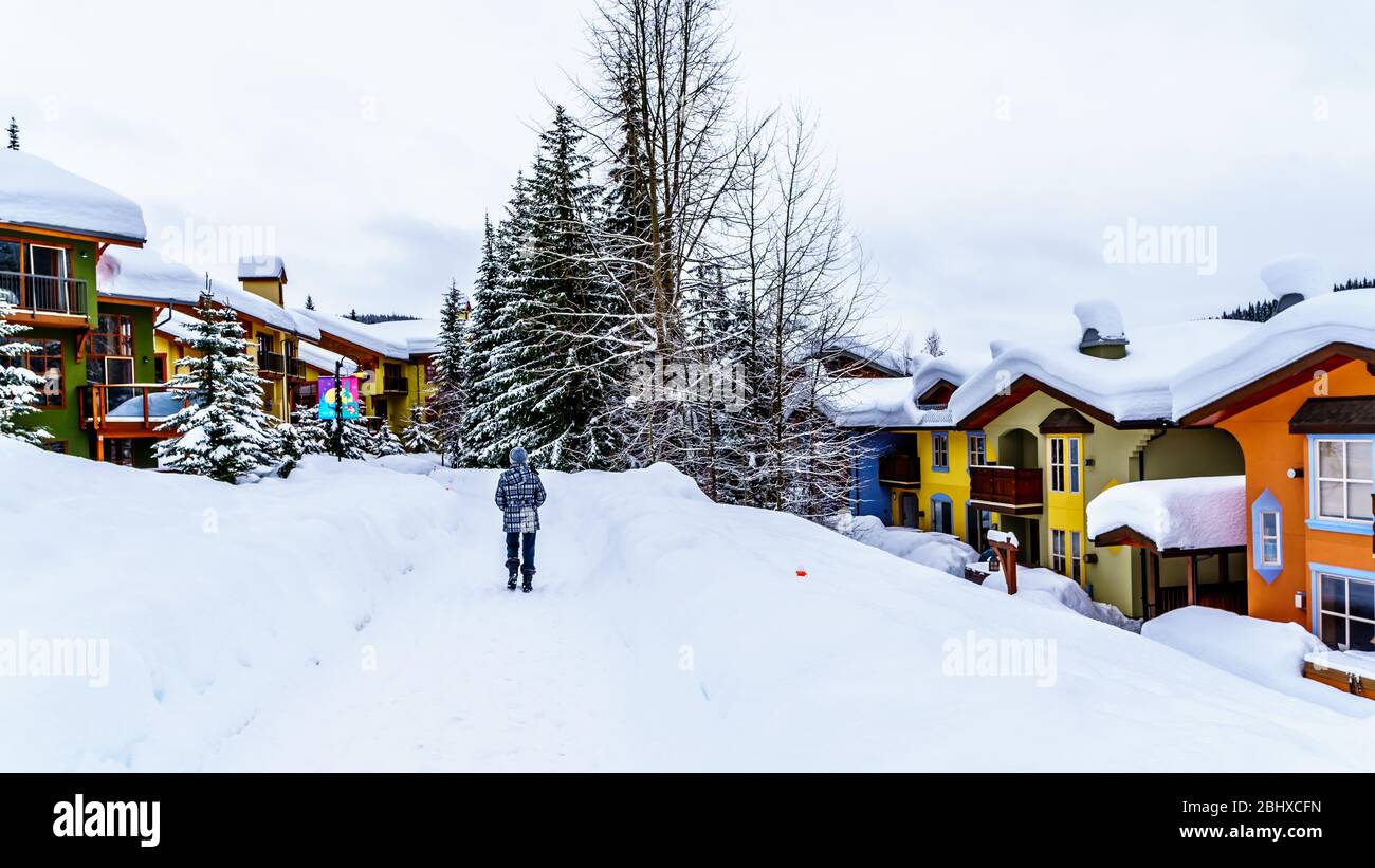 Camminando attraverso la neve lungo le case colorate nel Villaggio di Sun Peaks, un Villaggio Alpino nelle Highlands Shuswap di BC, Canada Foto Stock