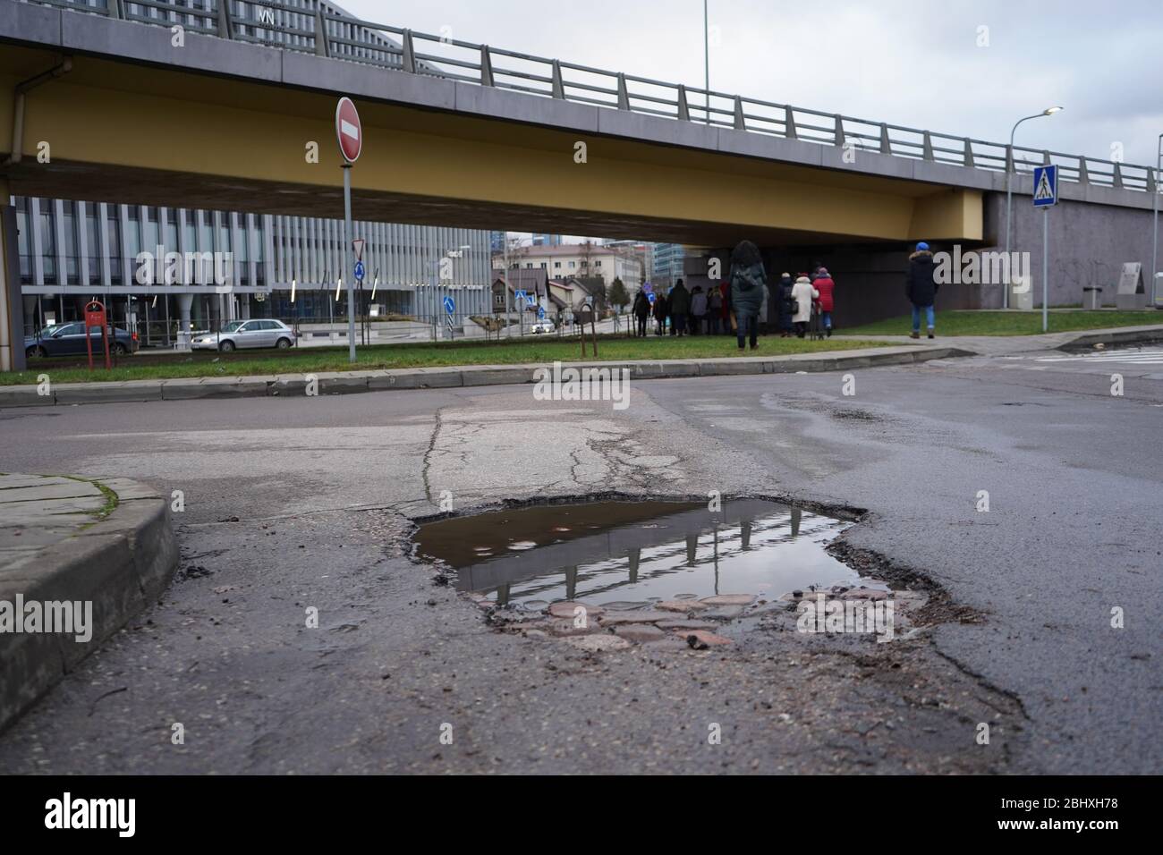 Strada con una pothole piena di acqua in città. La vecchia strada in pietra è visibile sotto l'asfalto. Foto Stock