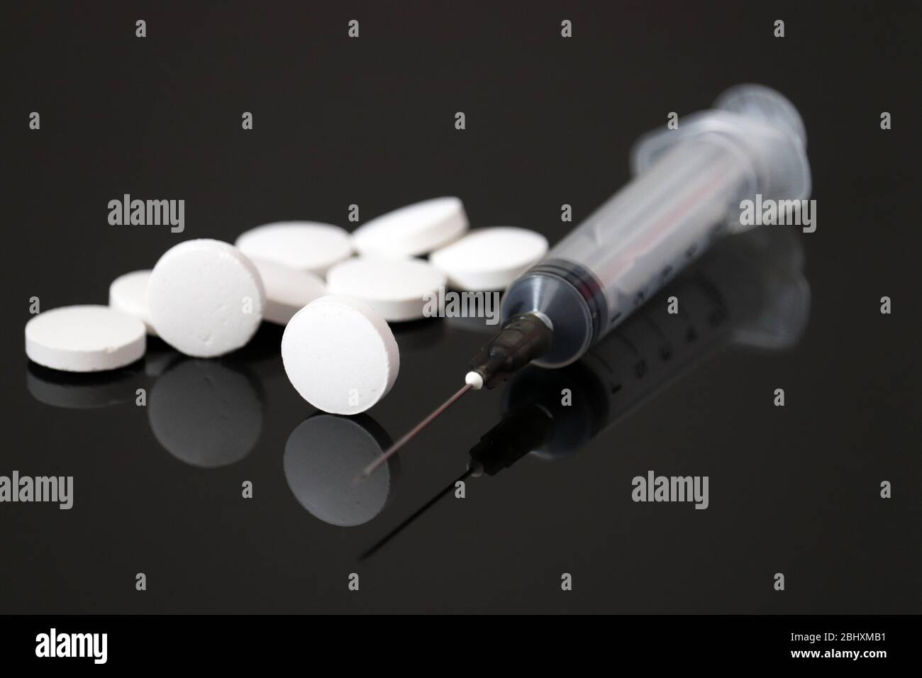 Pillole bianche e siringa su vetro scuro, compresse su sfondo nero. Concetto di iniezione di farmaco o vitamine Foto Stock