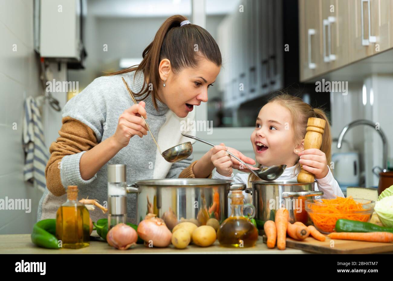 Madre emozionale e piccola figlia assaggiando insieme zuppa a casa Foto Stock