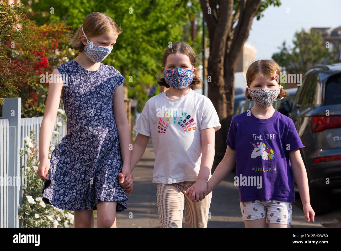 Tre giovani sorelle di cinque anni, 8 anni e 10 anni che indossano maschere che hanno fatto a casa con mamma da indossare durante la pandemia coronavirus COVID-19 / COVID 19 del 2020; maschera facciale casalinga. REGNO UNITO. (118) Foto Stock