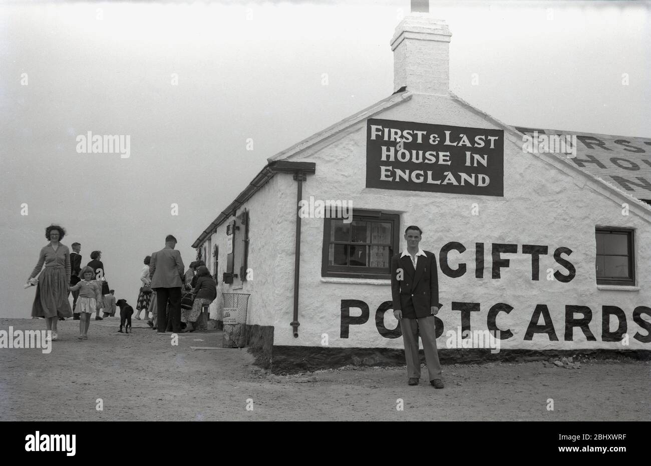 Anni '1950, storico, un gentiluomo con una camicia a colletto aperto, un blazer e pantaloni che rappresentano una foto all'esterno della famosa "First & Last House" a Lands End, Cornovaglia, un vecchio cottage su un solo piano che vendeva ai visitatori della costa, rinfreschi, regali, souvenir e cartoline, Inghilterra, REGNO UNITO. Foto Stock