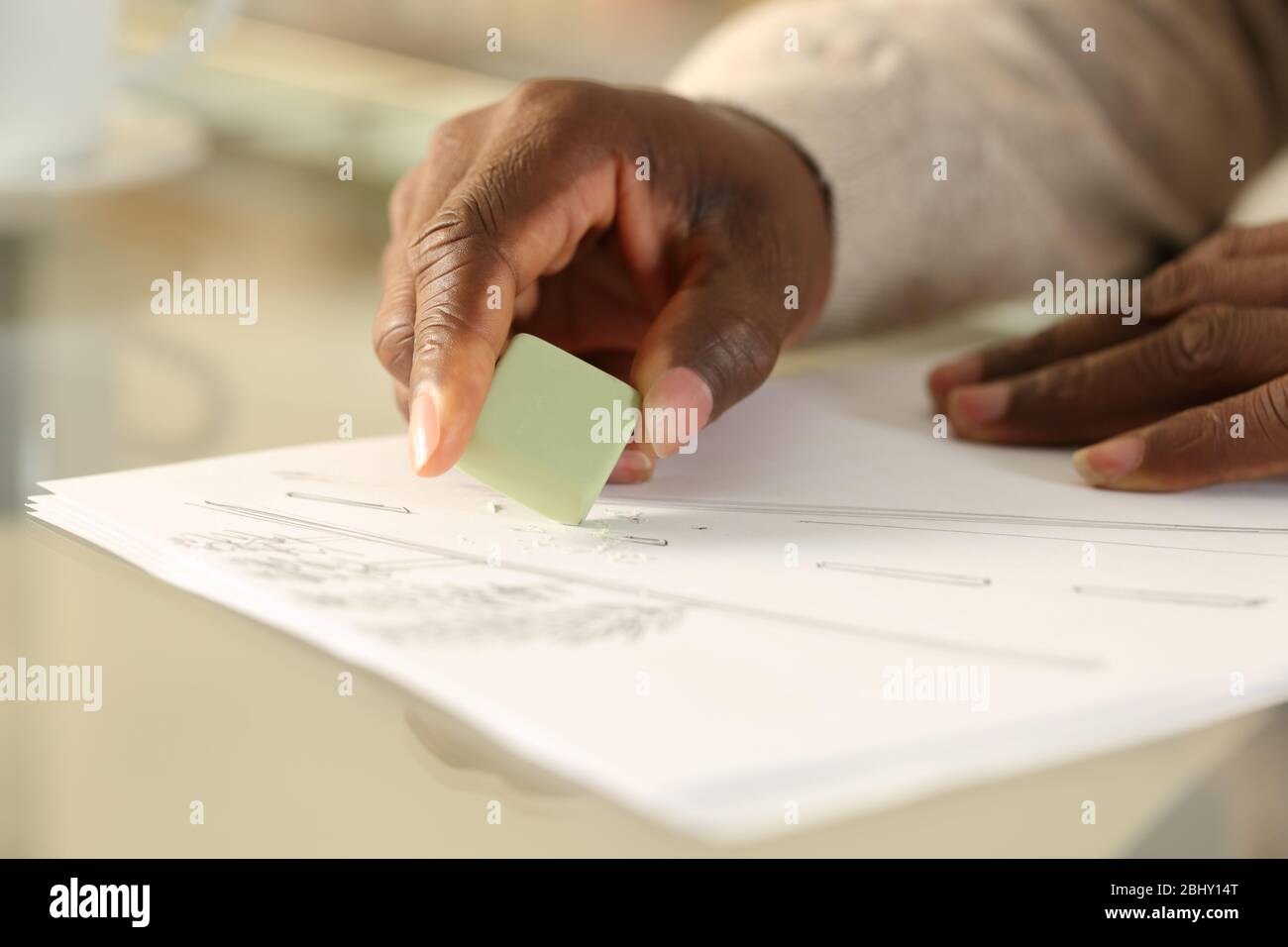 Primo piano delle mani nere cancellando disegno con gomma su una scrivania a casa Foto Stock