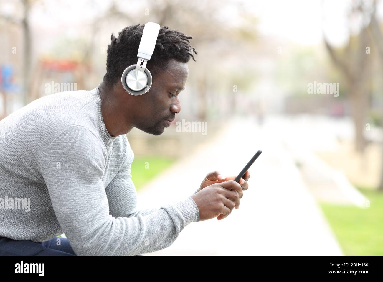 Profilo di un uomo nero serio con cuffie che ascoltano musica su smartphone  seduto su un panca di parco Foto stock - Alamy