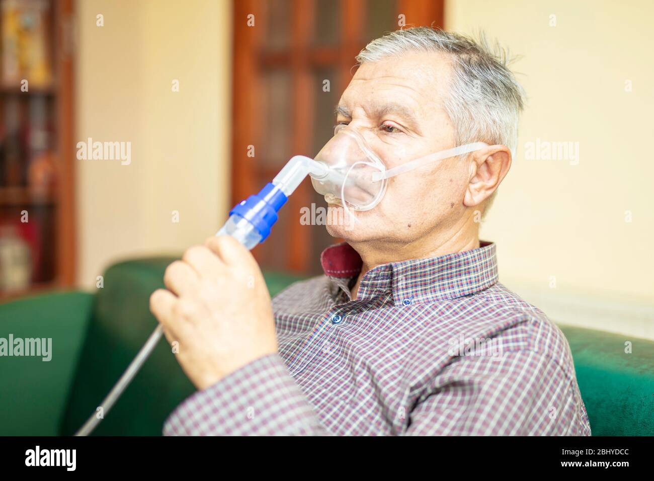 Uomo anziano che utilizza apparecchiature mediche per inalazione con maschera respiratoria e nebulizzatore nella stanza Foto Stock