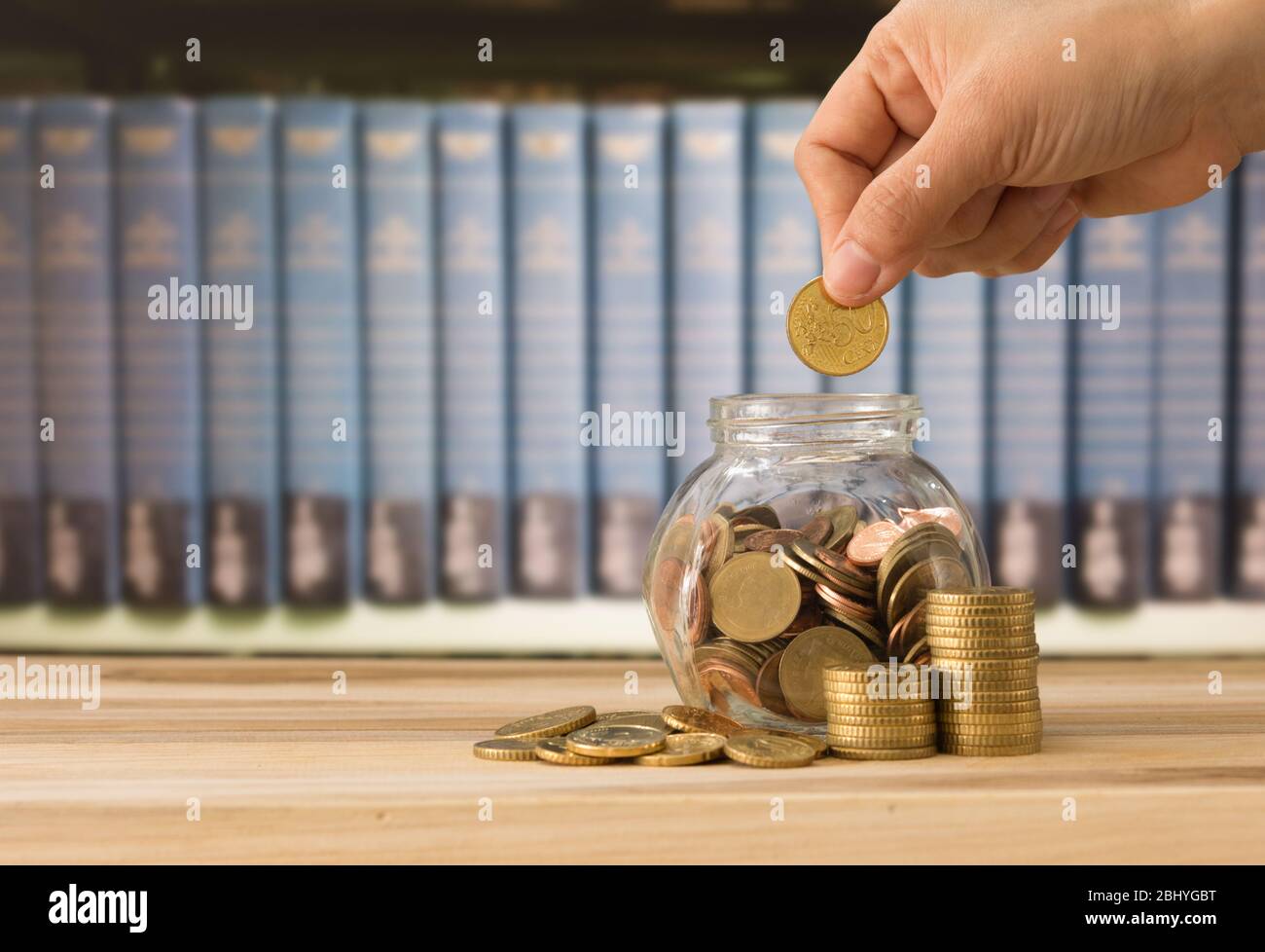 Mano mettendo monete in vaso con libreria in background. Concetto di risparmio per l'istruzione. Investire nel concetto di istruzione. Foto Stock
