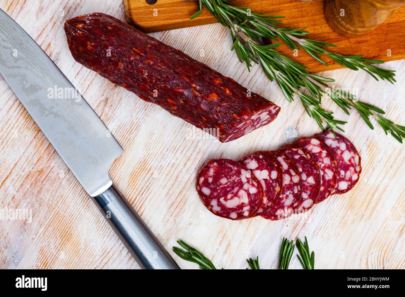 Salsiccia tradizionale tedesca di maiale semidicro e stagionato Braunschweiger tagliata su tagliere di legno con rosmarino e spezie Foto Stock