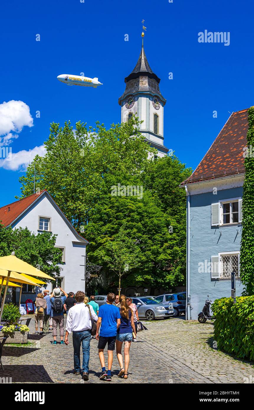 Scena urbana su Lingg Street con il campanile di Minster e la pubblicità zeppelin sopra la storica città vecchia di Lindau nel Lago di Costanza, Baviera, Germania. Foto Stock