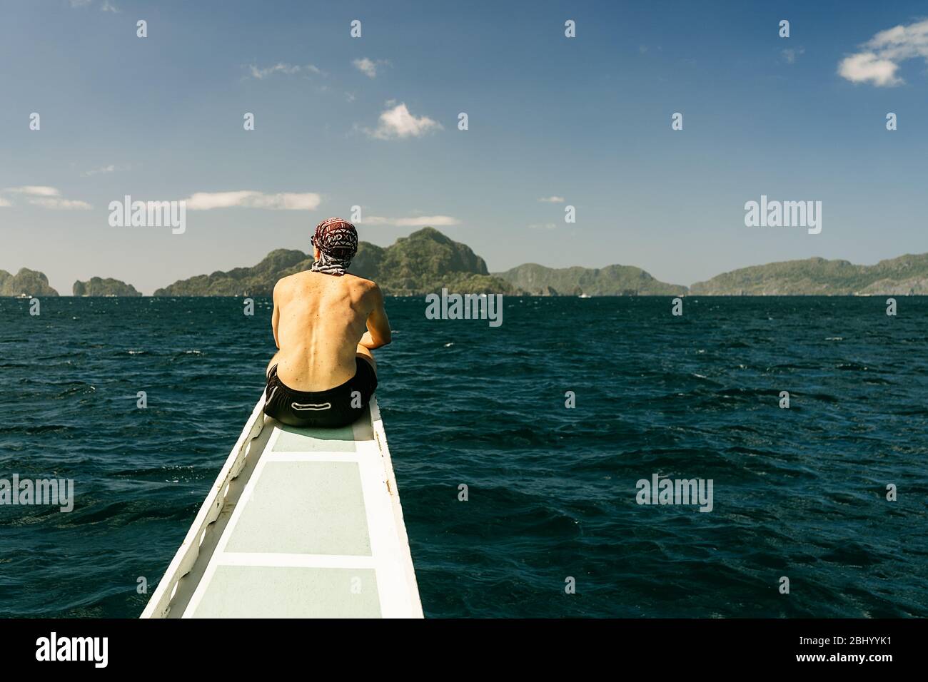 Uomo seduto sulla schiena a prua di una tradizionale barca filippina su un'isola che salta a El Nido, Palawan, Filippine. Verticale. Foto Stock