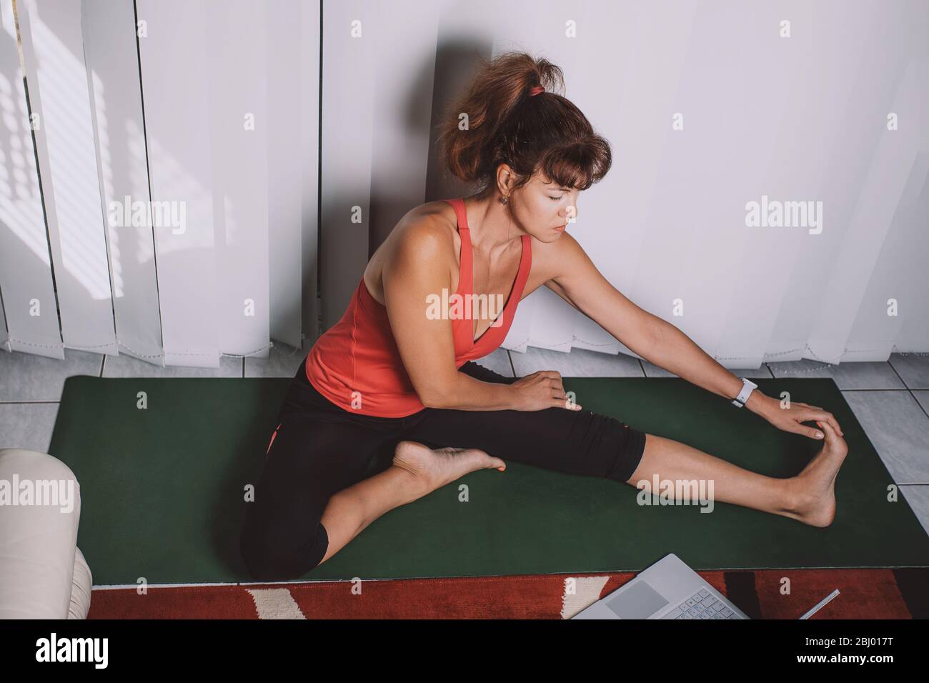 Attraente donna di mezza età che fa yoga a casa, avendo lezione online. Mantenete la salute durante il blocco della quarantena. Foto Stock