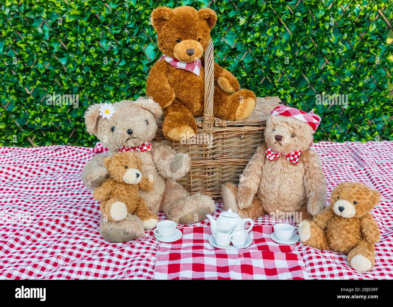 Picnic di Teddy Bear. Cinque orsacchiotti che si godono un pic-nic nel giardino con il panno da tavolo rosso e bianco di gingham e teacups bianco cina. Concetto: Felice Foto Stock