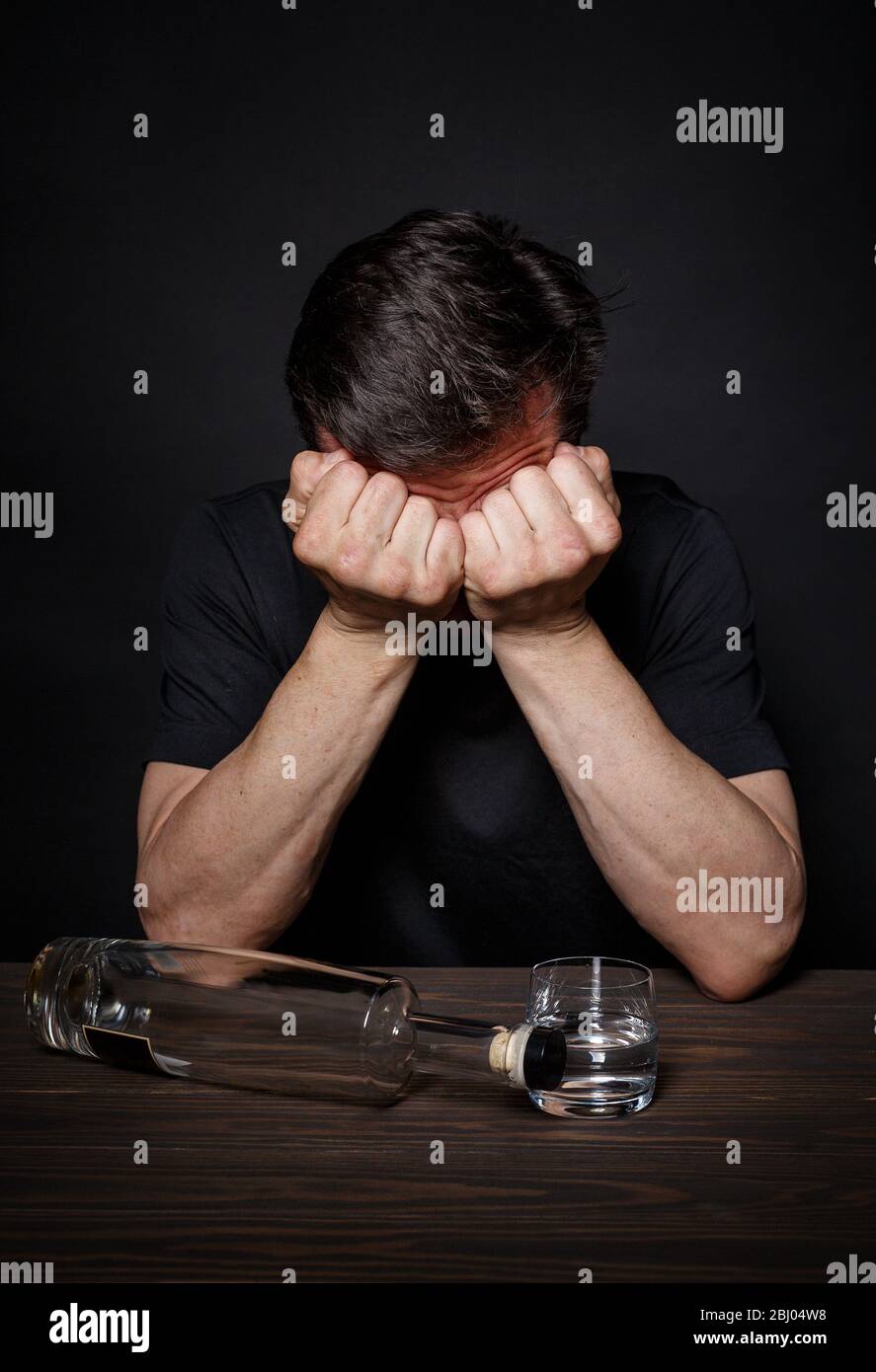 L'uomo con una dipendenza da alcol siede a un tavolo in disperazione Foto Stock