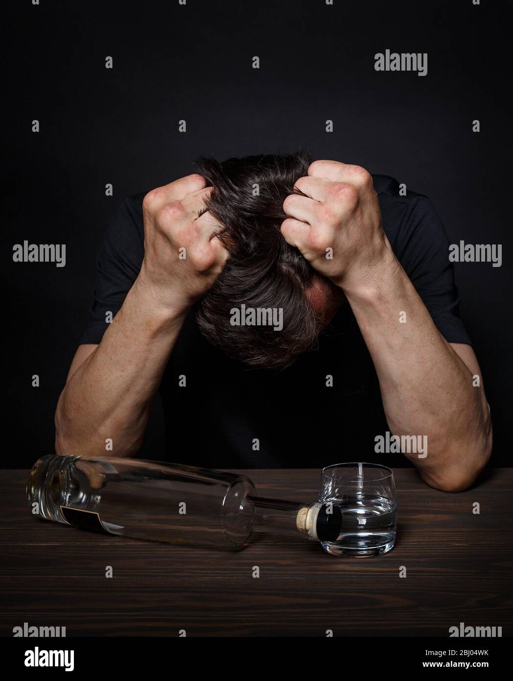 L'uomo con una dipendenza da alcol siede a un tavolo in disperazione Foto Stock
