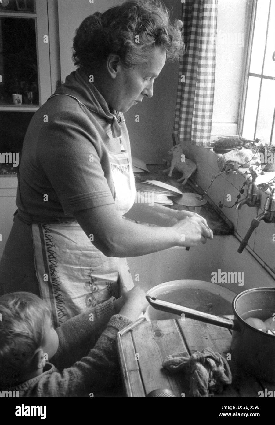 Casalinga e madre che spellano le patate al lavandino della cucina. 1955 Foto Stock