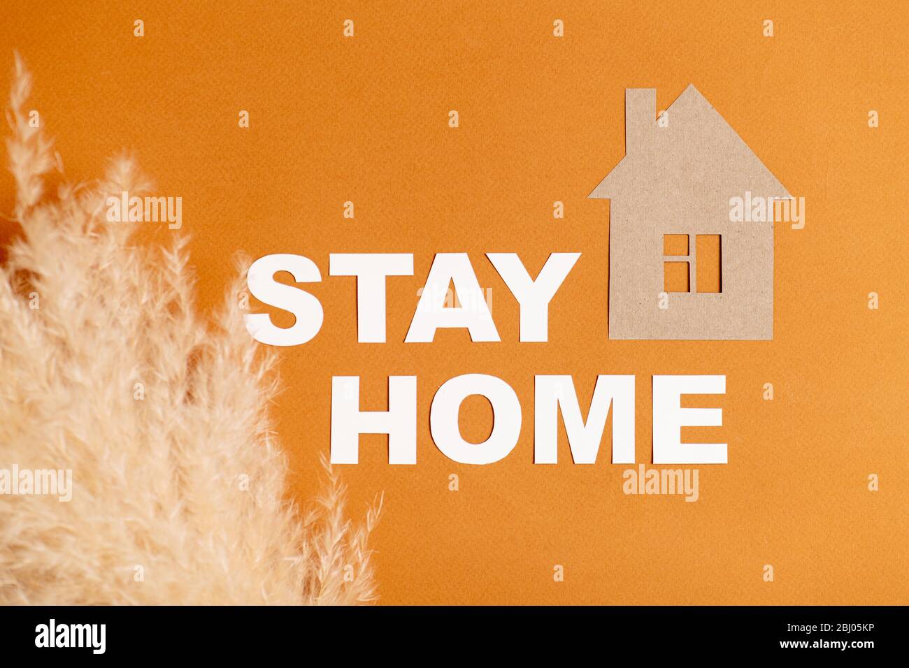 Composizione del messaggio di soggiorno a casa con la casa di carta e le orecchie di cereali su arancione Foto Stock