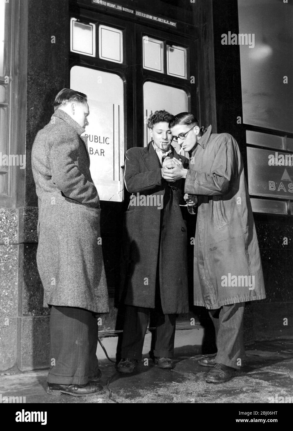 Uomini in piedi fuori porte di bar pubblico che hanno una sigaretta - Foto Stock